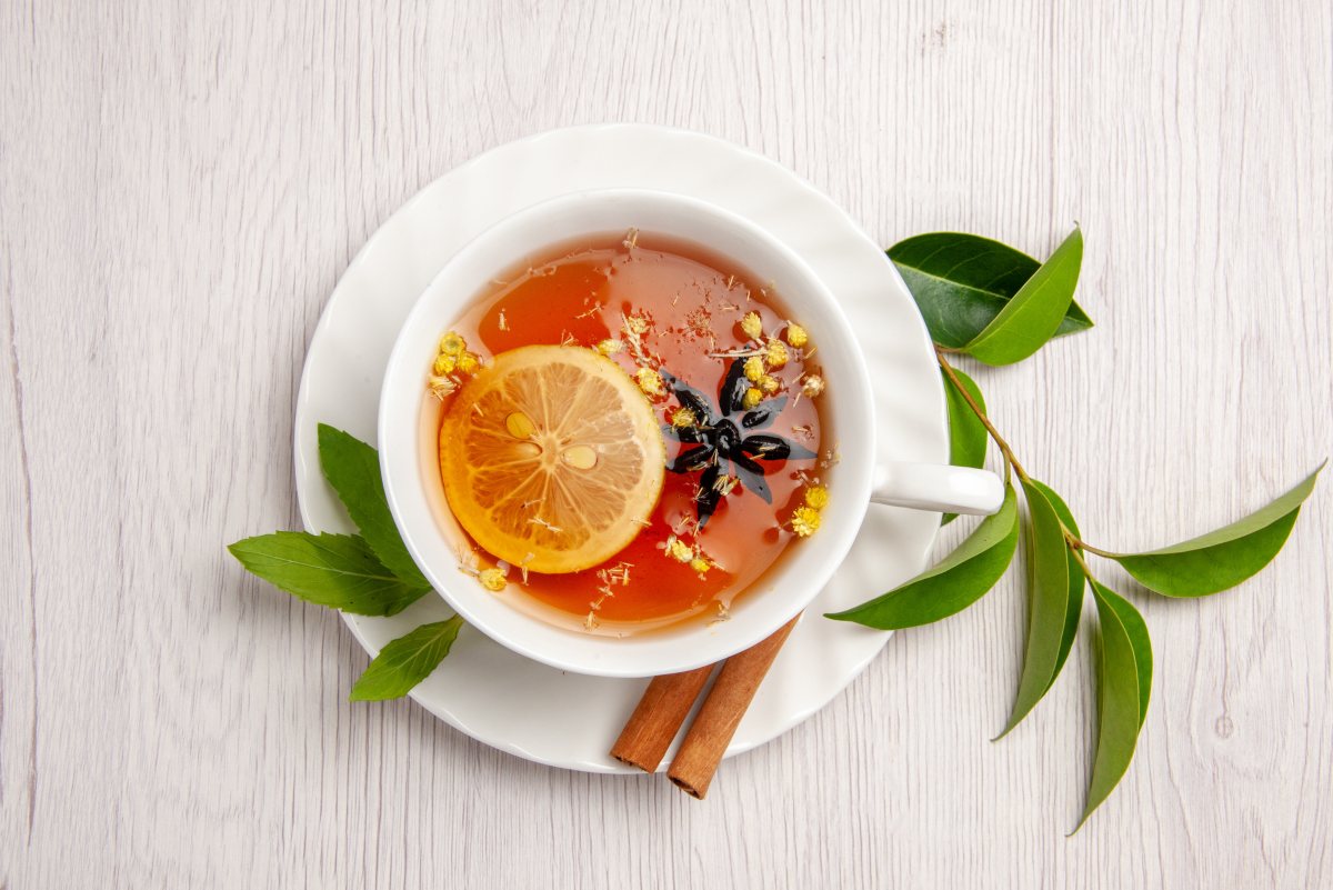 top-close-up-view-herbal-tea-a-cup-of-herbal-tea-with-lemon-and-cinnamon-sticks-on-the-white-saucer-and-tea-leaves