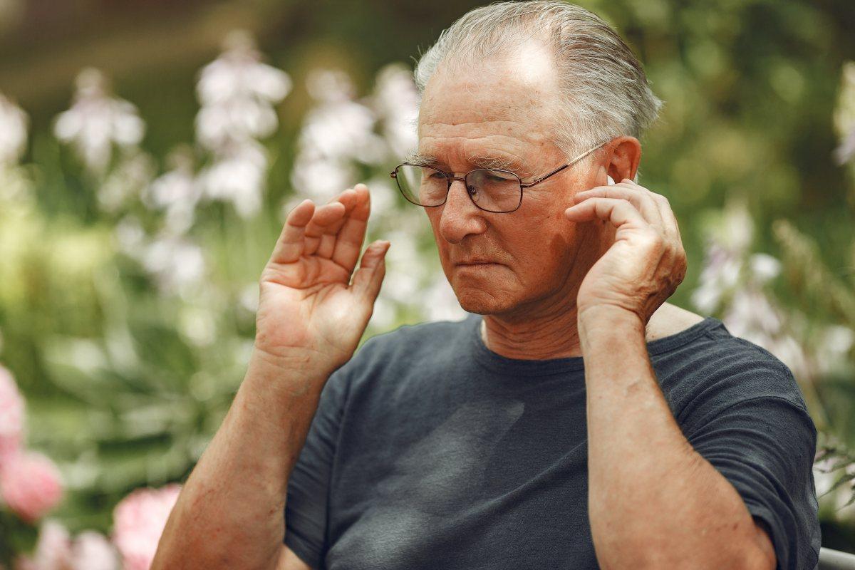 starszy mężczyzna wkłada do ucha aparat słuchowy