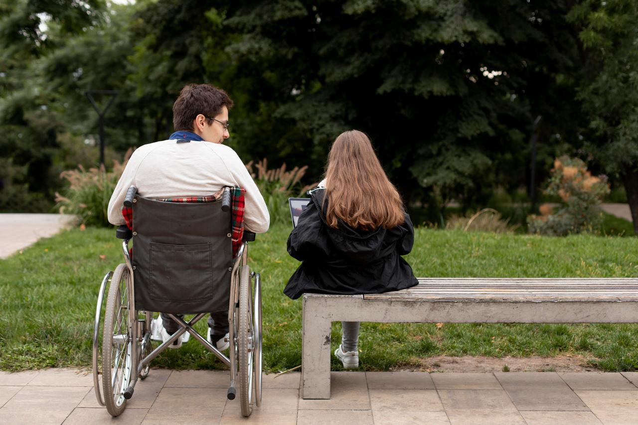 niepełnosprawny mężczyzna na wózku inwalidzkim obok dziewczyny na ławce
