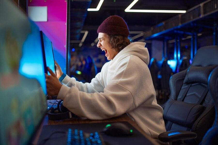 młody podekscytowany chłopak gra na komputerze siedząc na fotelu gamera
