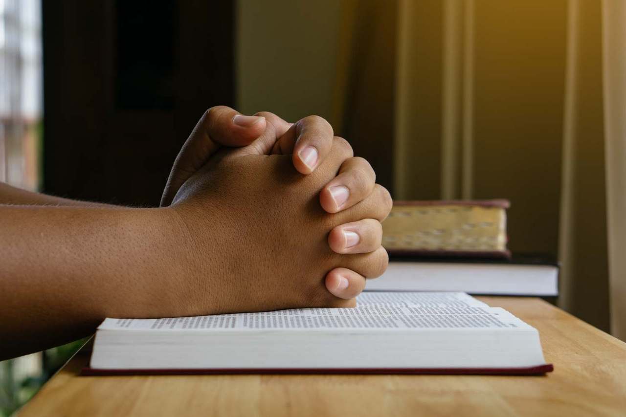 dłonie złożone do modlitwy spoczywają na modlitewniku
