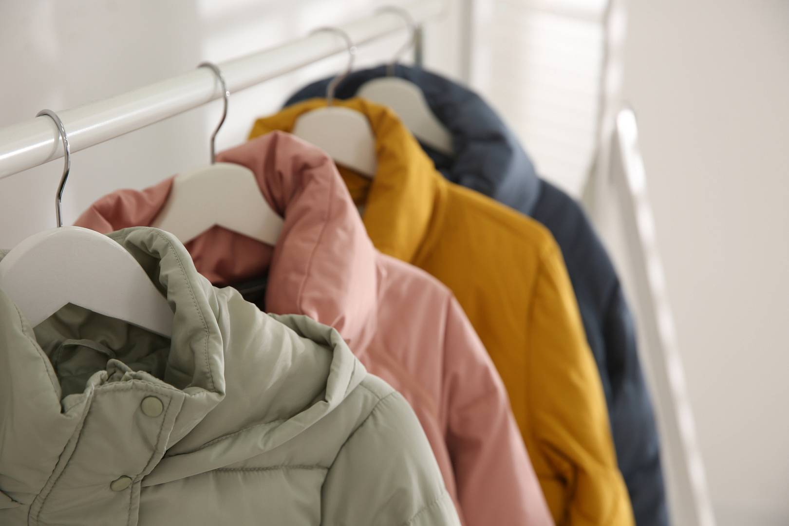 Different warm jackets hanging on rack indoors, closeup