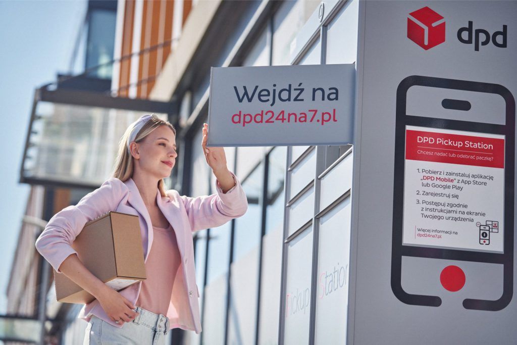 Kobieta w jasnoróżowej marynarce, trzymająca paczkę i korzystająca z automatu paczkowego DPD Pickup. Na automacie widnieje reklama strony dpd24na7.pl, zachęcająca do wygodnego odbioru paczek jesienią.
