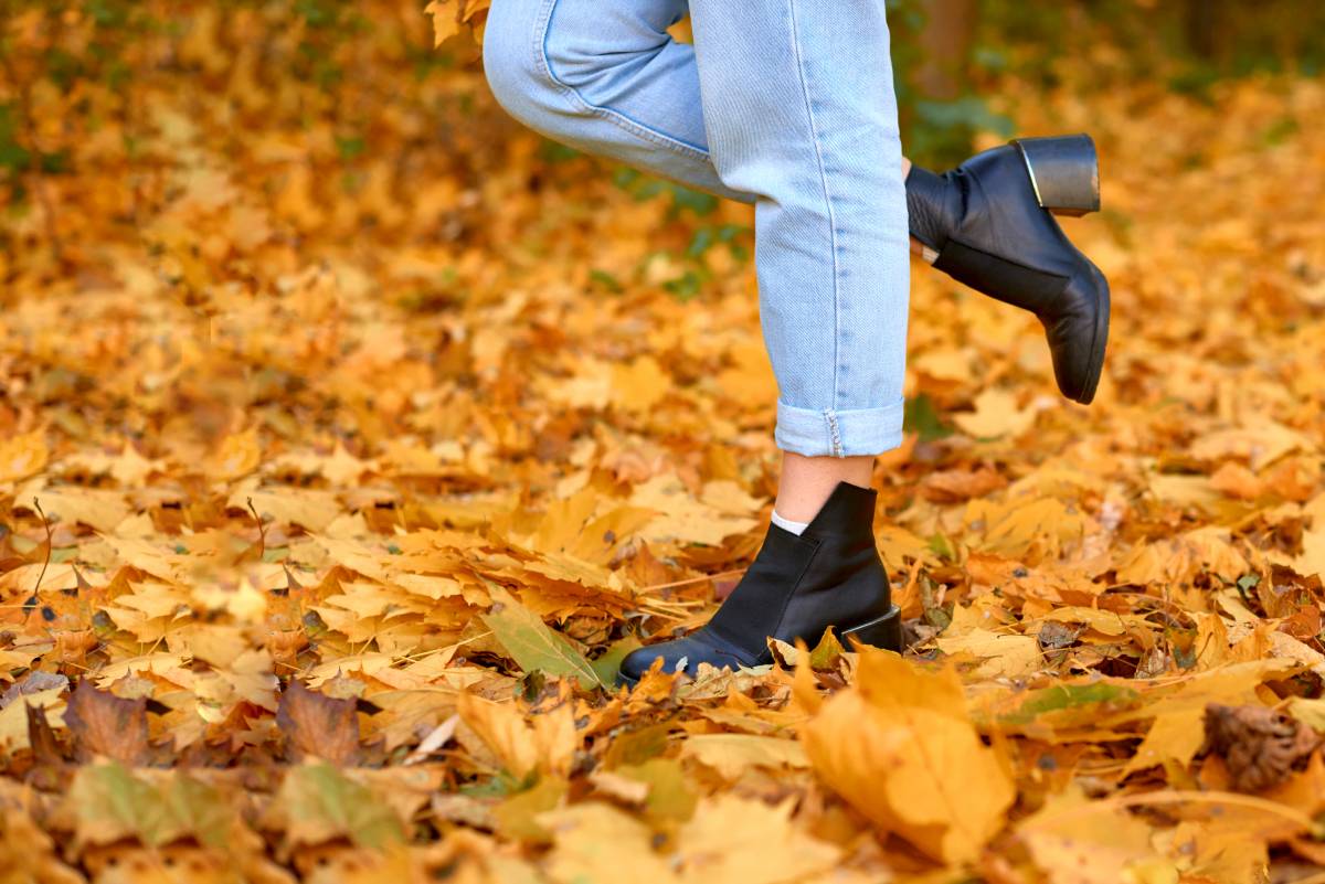 woman's slender legs in jeans and boots stand in fallen leaves. copy space. shallow depth of field