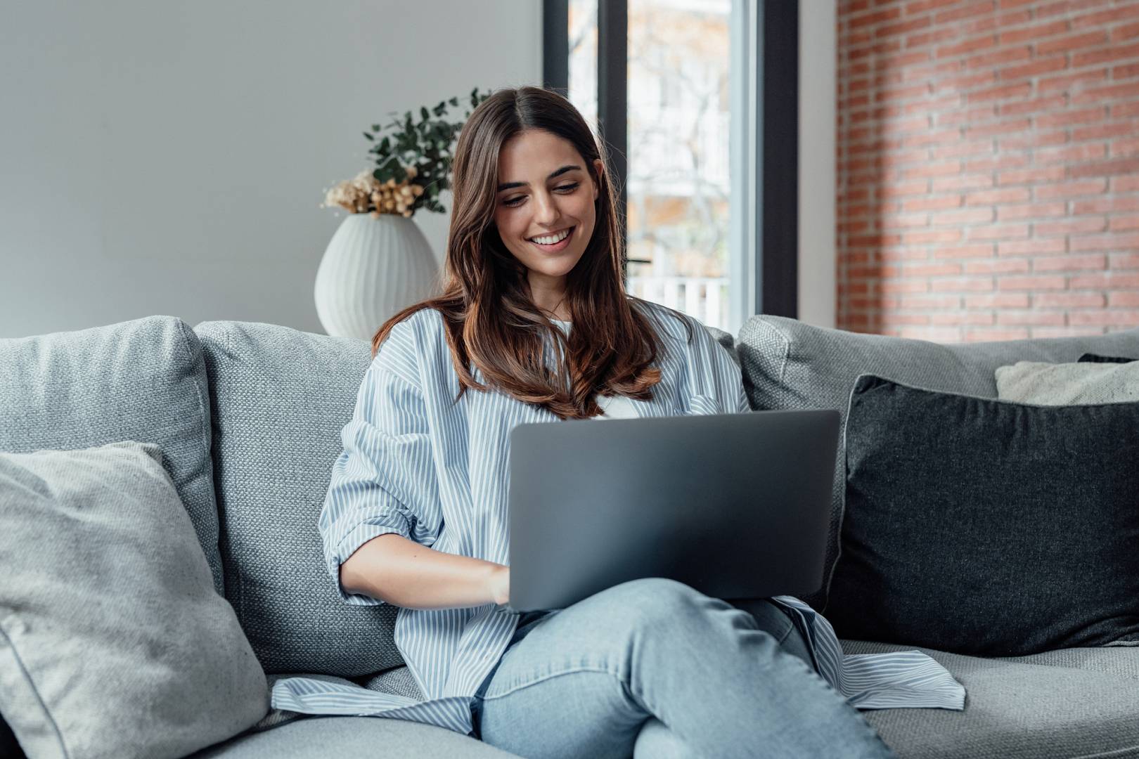 Concentrated millennial girl sit on couch working on laptop brow