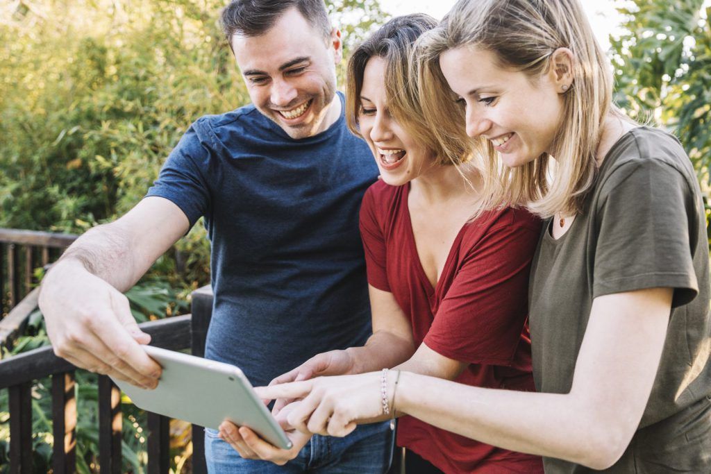 cheerful friends using tablet near fence