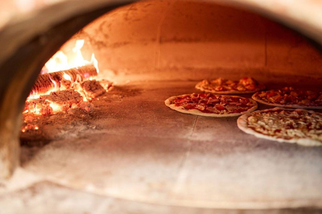 duży piec ogrodowy opalany drewnem z czterema pizzami w środku
